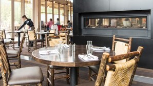 A restaurant with round tables, wooden chairs, and a large window overlooking the street.