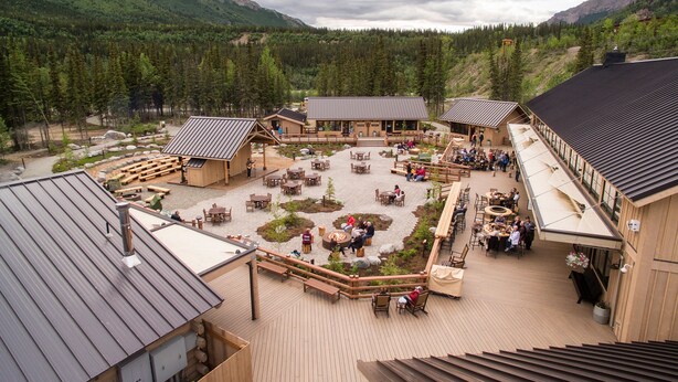 A lodge with outdoor seating areas, a central gathering space, and a view of the surrounding forest and mountains.