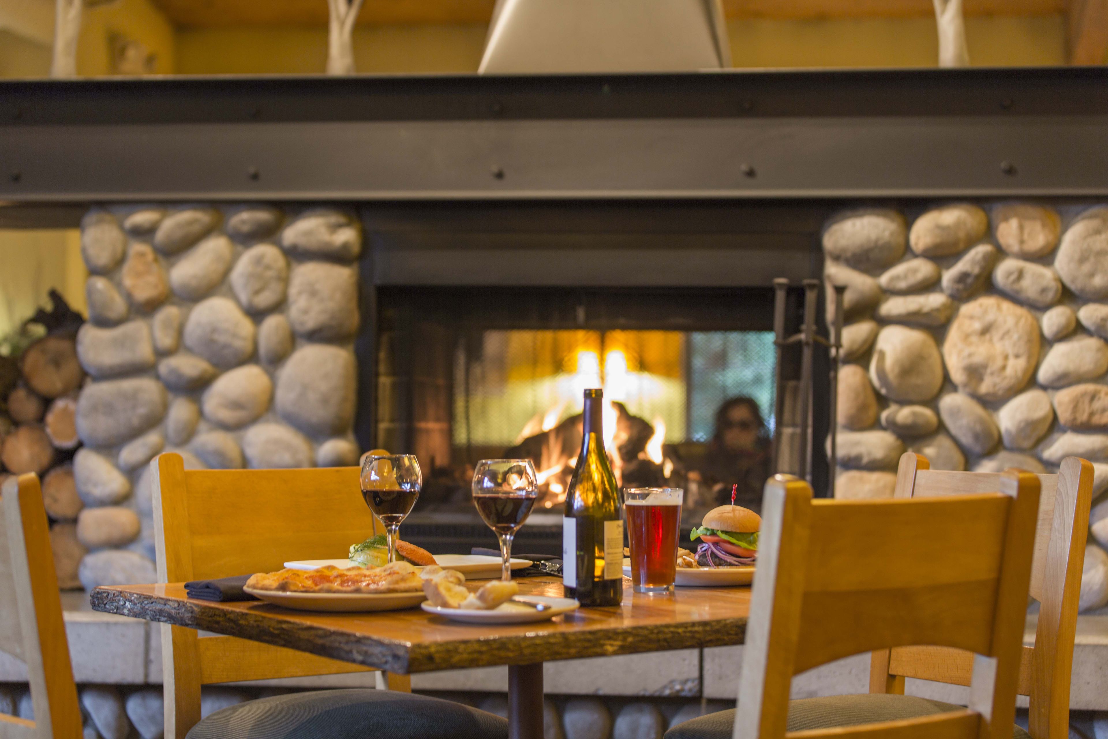 Una mesa de comedor con platos de comida, vasos y una botella, frente a una pared de piedra con chimenea.