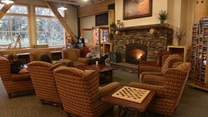 A cozy lounge area with wicker furniture, a fireplace, and a bookshelf. - Denali Park Village (Denali National Park)