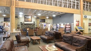 A spacious lobby with wooden furniture, a fireplace, and a stone wall. - Denali Park Village (Denali National Park)
