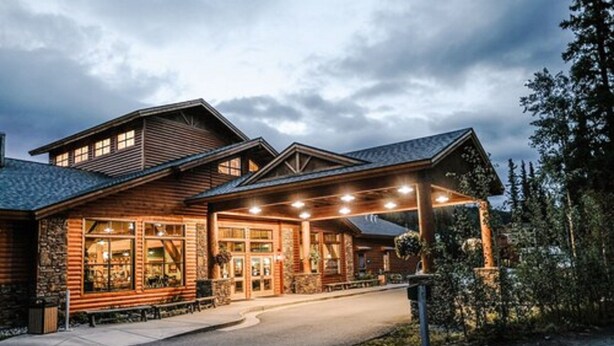 A log cabin-style hotel with a covered entrance, large windows, and a stone facade. - Denali Park Village (Denali National Park)