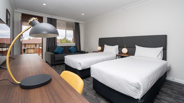 A hotel room with two beds, a desk, a chair, a lamp, and a view of the outside. - Littomore Suites Bathurst (Bathurst)