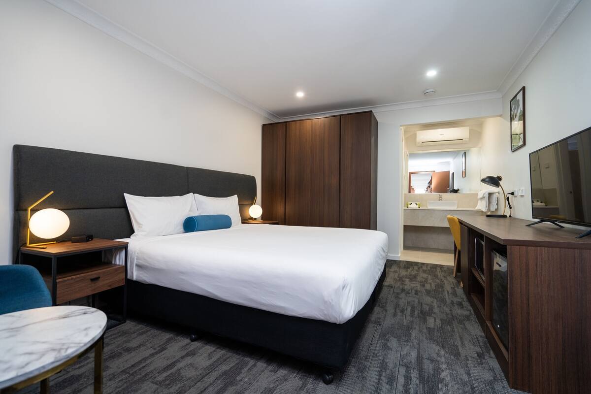 A hotel room with a large bed, bedside tables, a desk, a chair, and a television.