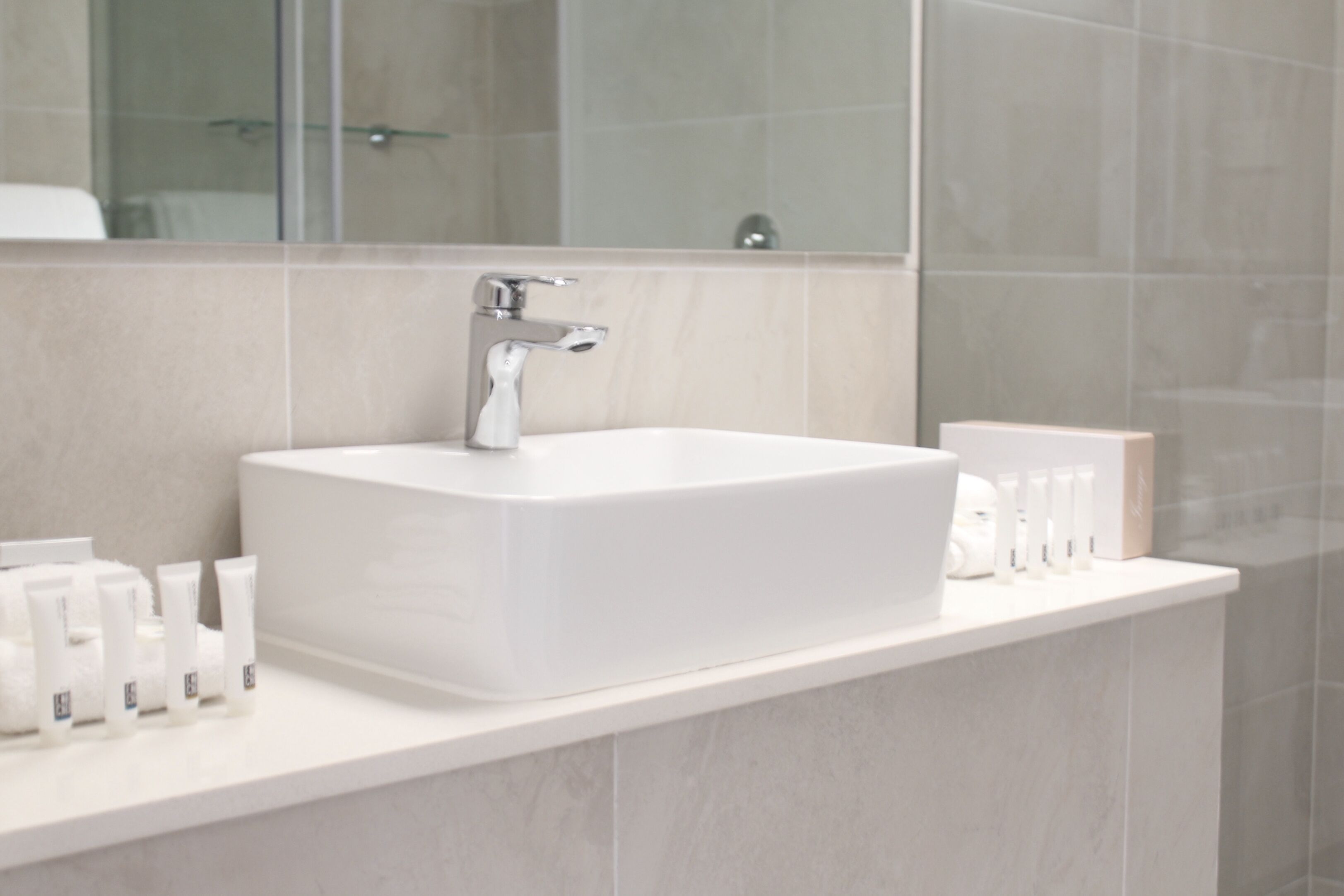 Une salle de bain moderne avec un grand lavabo blanc, un miroir et des articles de toilette posés sur le comptoir.