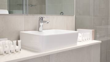 A modern bathroom with a large white sink, a mirror, and toiletries on the countertop.