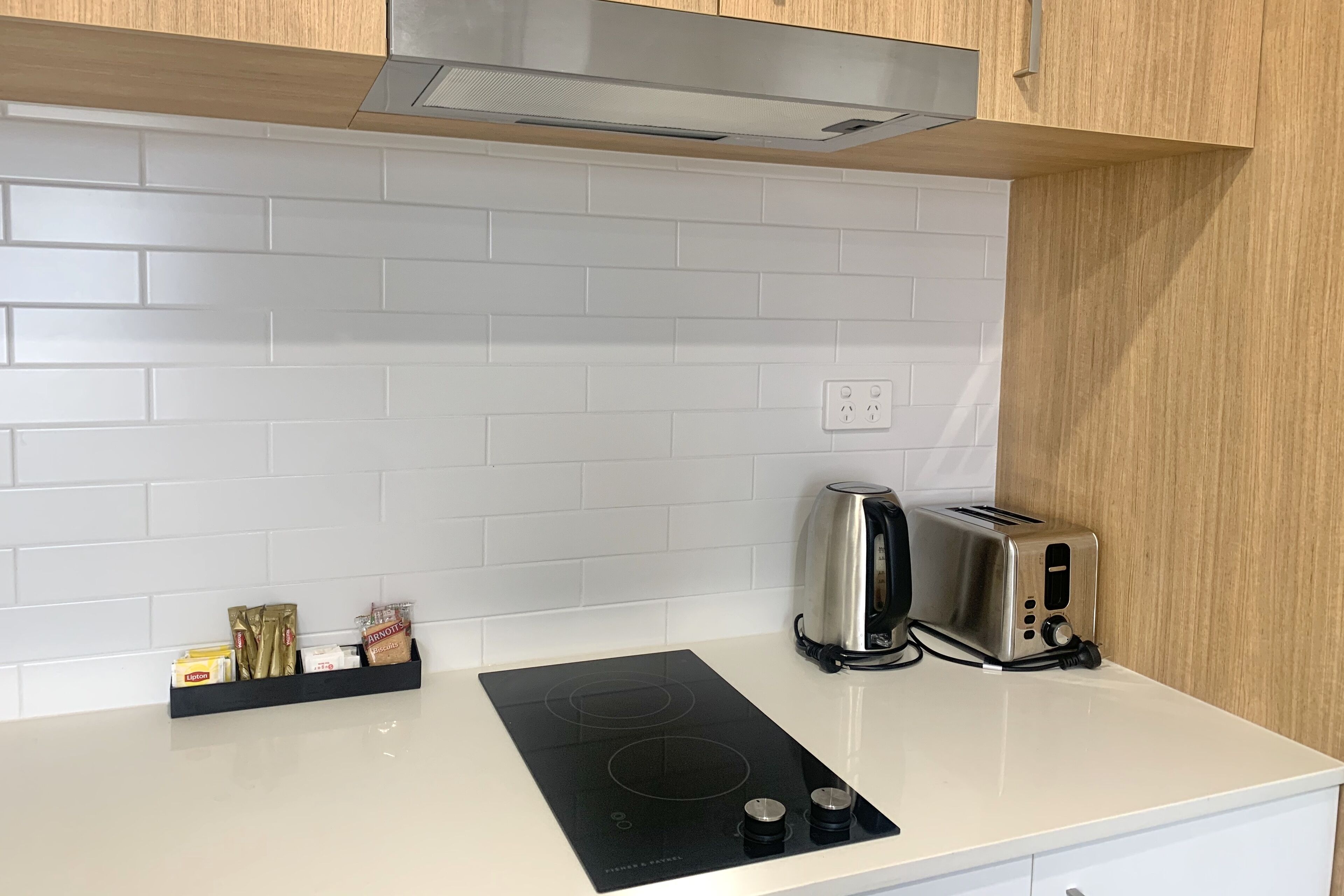 A kitchen with a white countertop, a black induction cooktop, a toaster, and a stainless steel kettle.