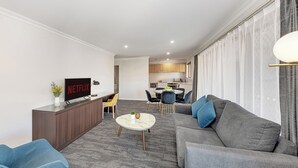 A modern living room with a grey sofa, a coffee table, and a TV displaying 'NETFLIX'. - Littomore Suites Bathurst (Bathurst)