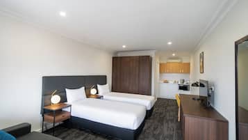 Habitación de hotel con dos camas, un escritorio, una silla, un pequeño sofá y una kitchenette al fondo.