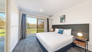 A hotel room with a large bed, a bedside table with a lamp, and a view of the outdoors through a sliding door. - Littomore Suites Bathurst (Bathurst)