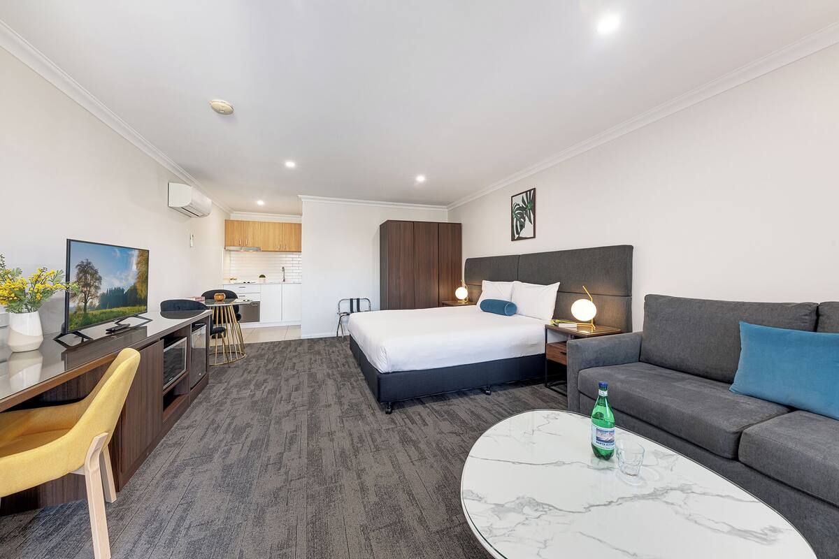A hotel room with a bed, sofa, desk, and a dining area.