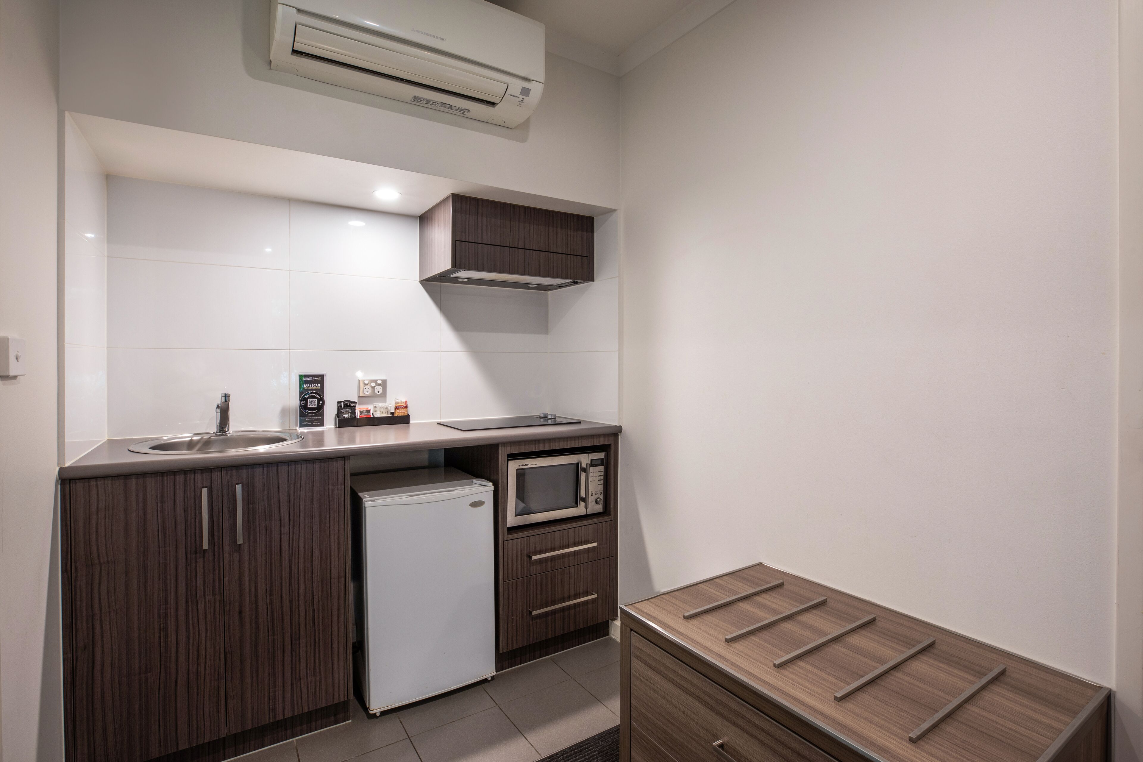 Una cocina compacta con microondas integrado, un refrigerador pequeño y un gabinete de madera.