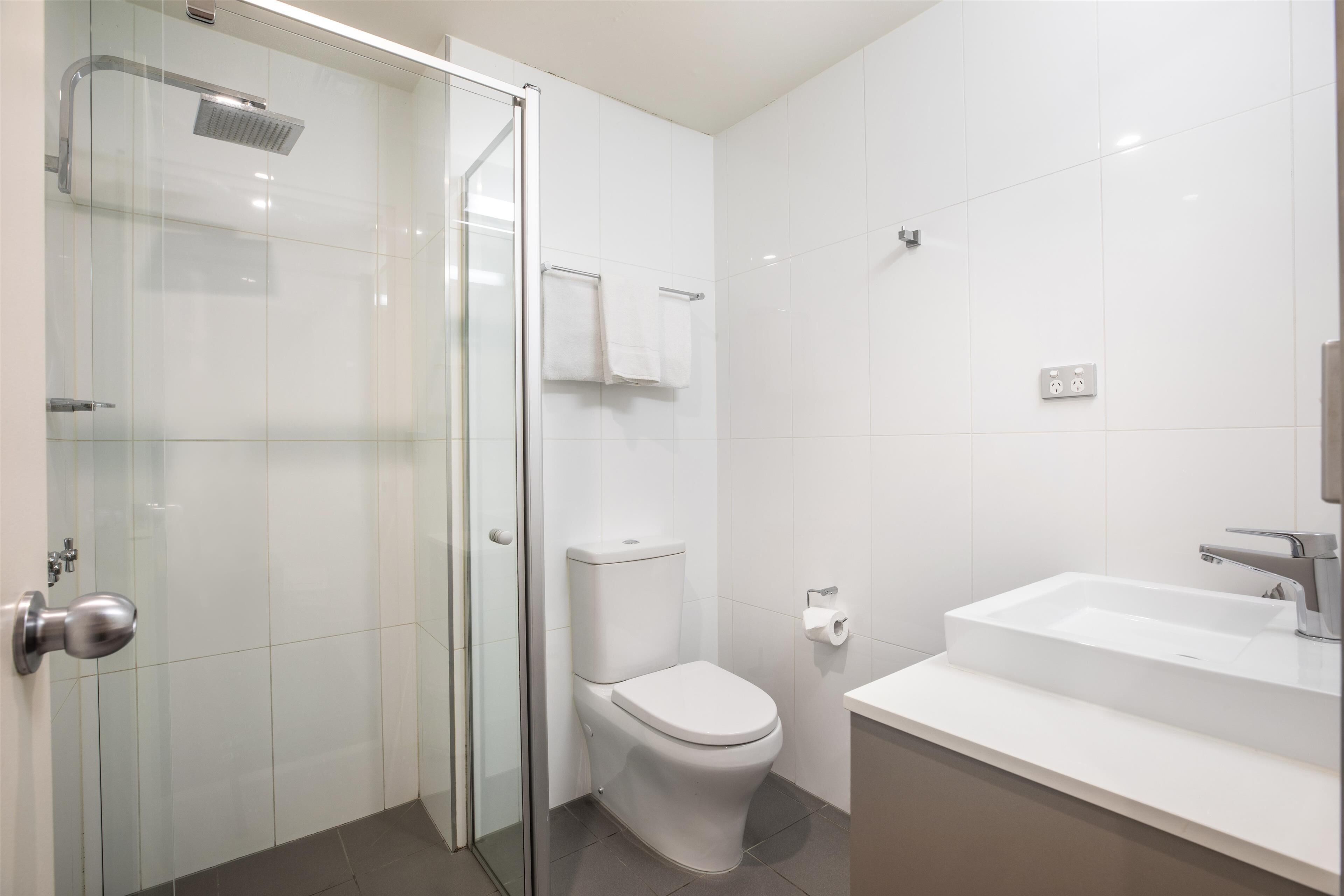 Een moderne badkamer met een glazen douchecabine, een toilet en een wastafel met spiegel.
