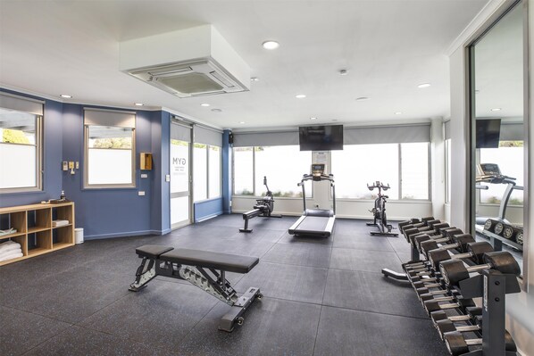 A gym with exercise equipment, a bench, and a wall-mounted TV.
