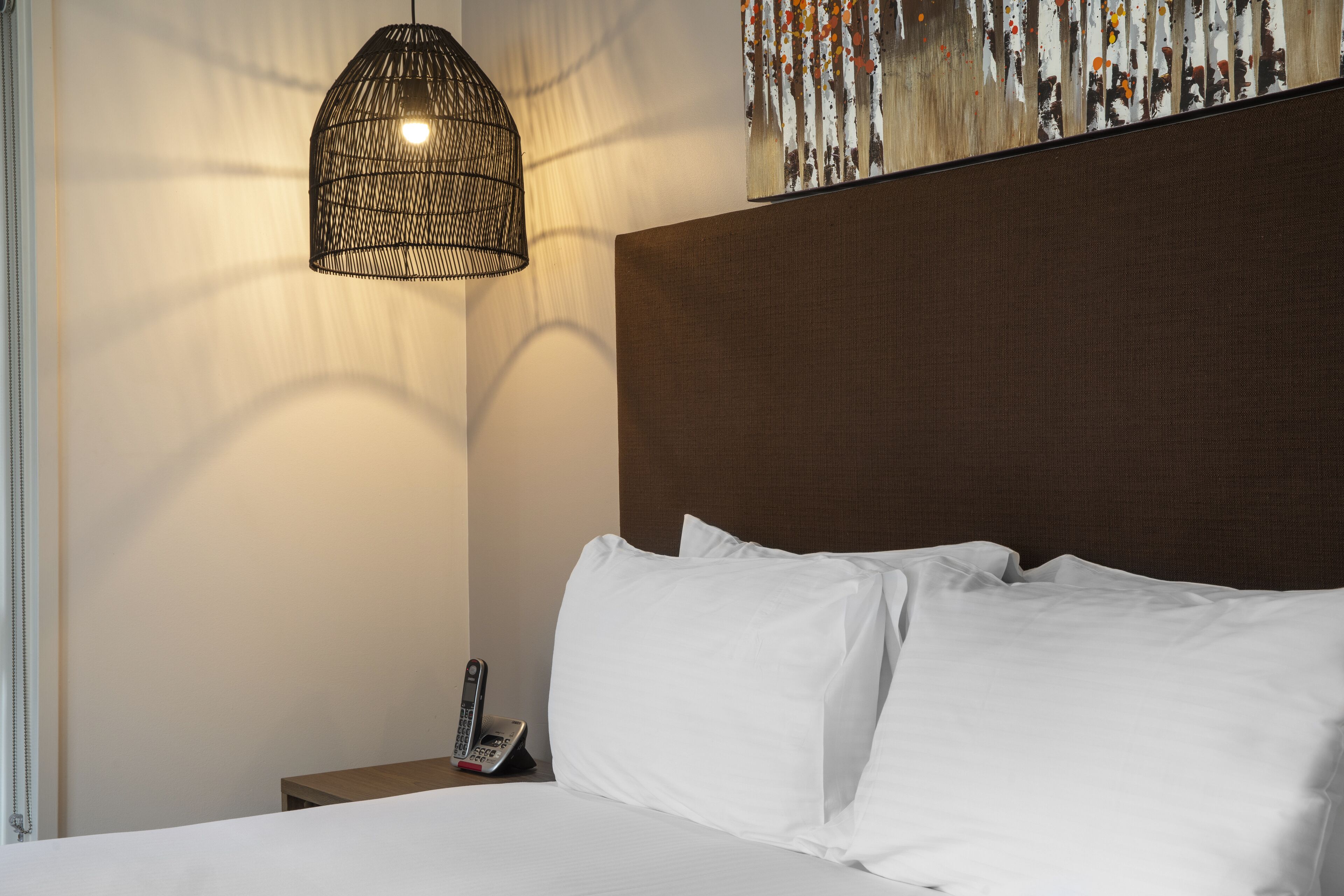 A neatly made bed with white linens, a hanging light fixture, and a telephone on a bedside table.
