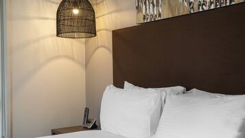 A neatly made bed with white linens, a hanging light fixture, and a telephone on a bedside table.