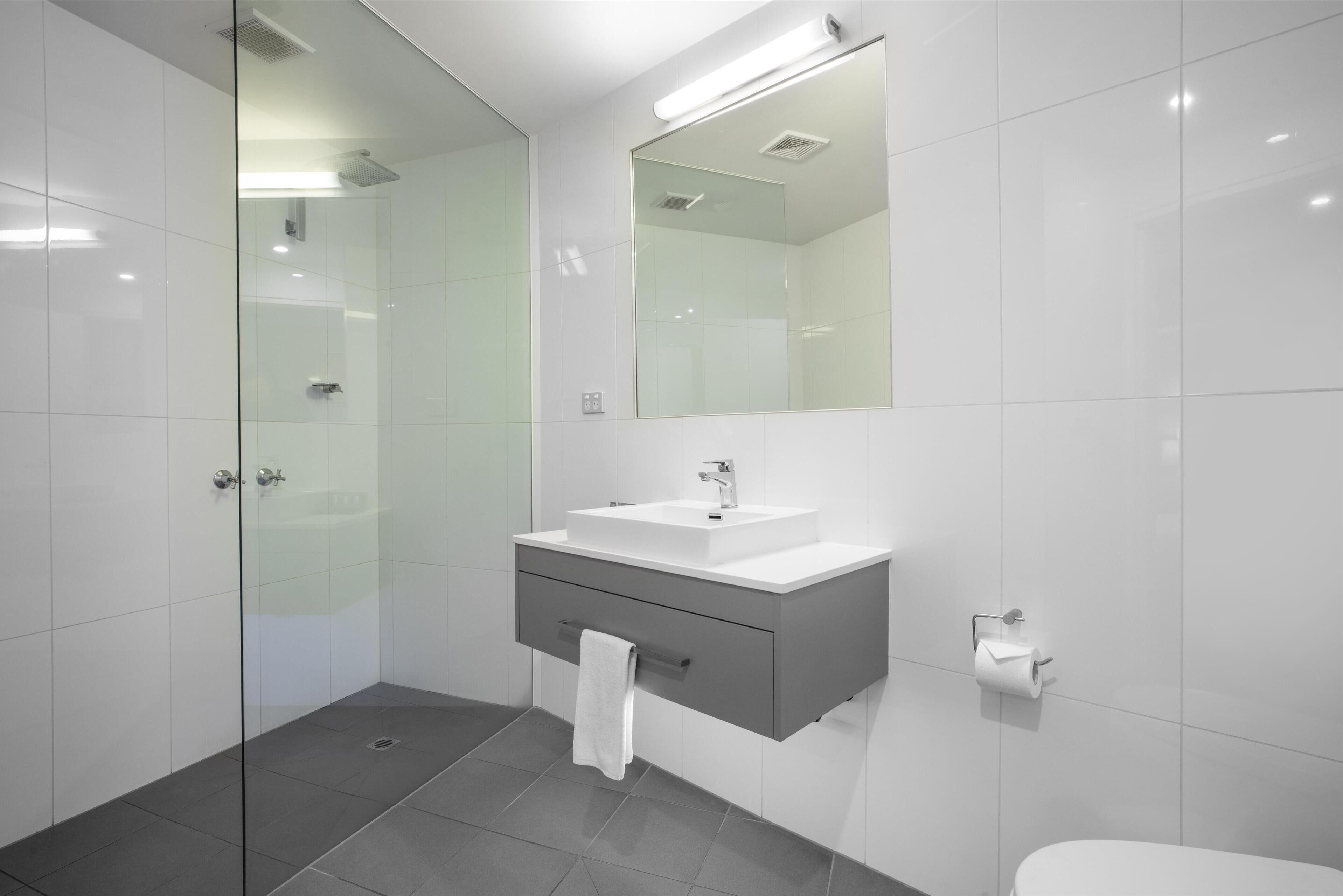 Een moderne badkamer met een douchecabine van glas, een witte wastafel met spiegel erboven en een toilet.
