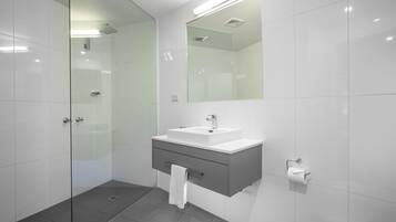 Een moderne badkamer met een douchecabine van glas, een witte wastafel met spiegel erboven en een toilet.