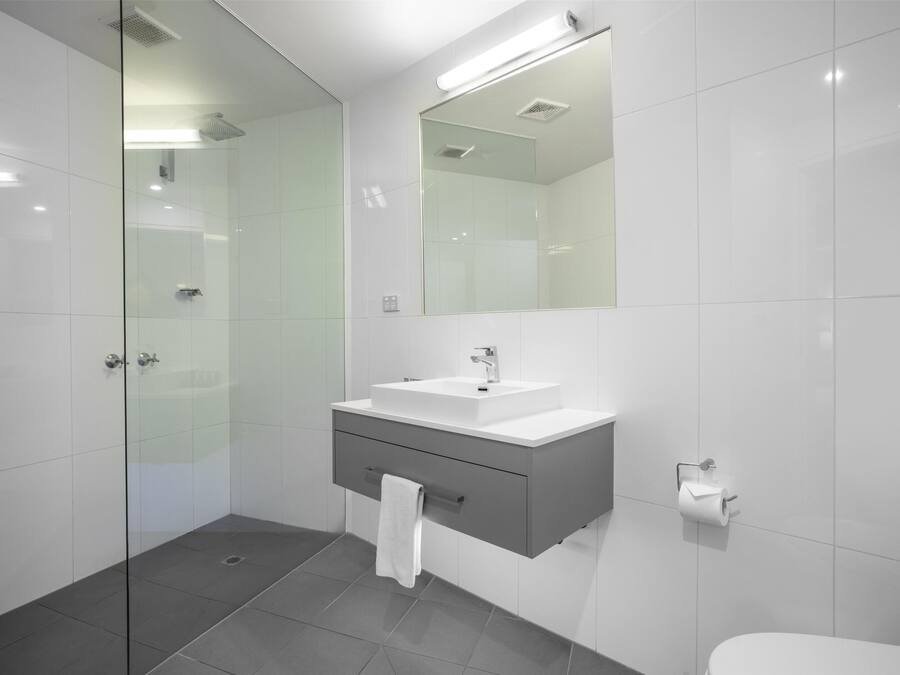 Een moderne badkamer met een douchecabine van glas, een witte wastafel met spiegel erboven en een toilet.