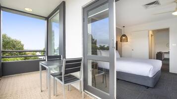 A hotel room with a bed, a glass door leading to a balcony, a small table, and a chair.