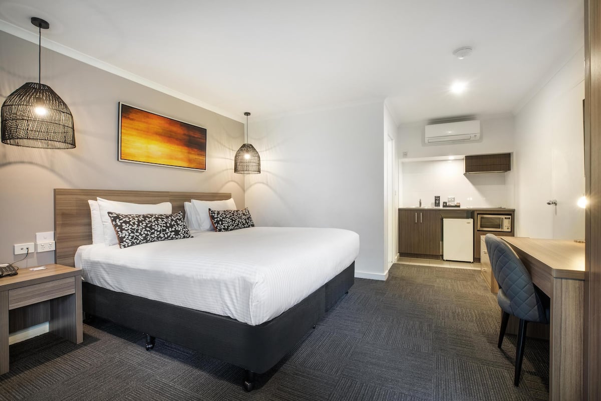 Ein Hotelzimmer mit Bett, Nachttisch und Schreibtisch mit Stuhl. Es gibt eine Küchenzeile inklusive Mikrowelle und Kühlschrank.