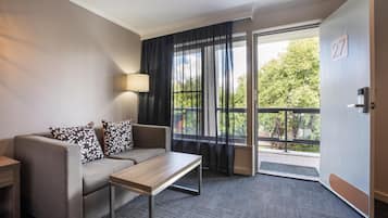 A hotel room with a sofa, a small table, a lamp, a sliding glass door to an outdoor balcony, and a door with the number 27.