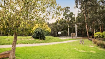 Um parque com um caminho pavimentado, uma placa com o texto 'Guests of the Court' e diversas árvores e arbustos.