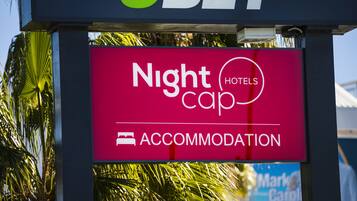 Señal de Nightcap Hotels con una vista despejada de palmeras al fondo.
