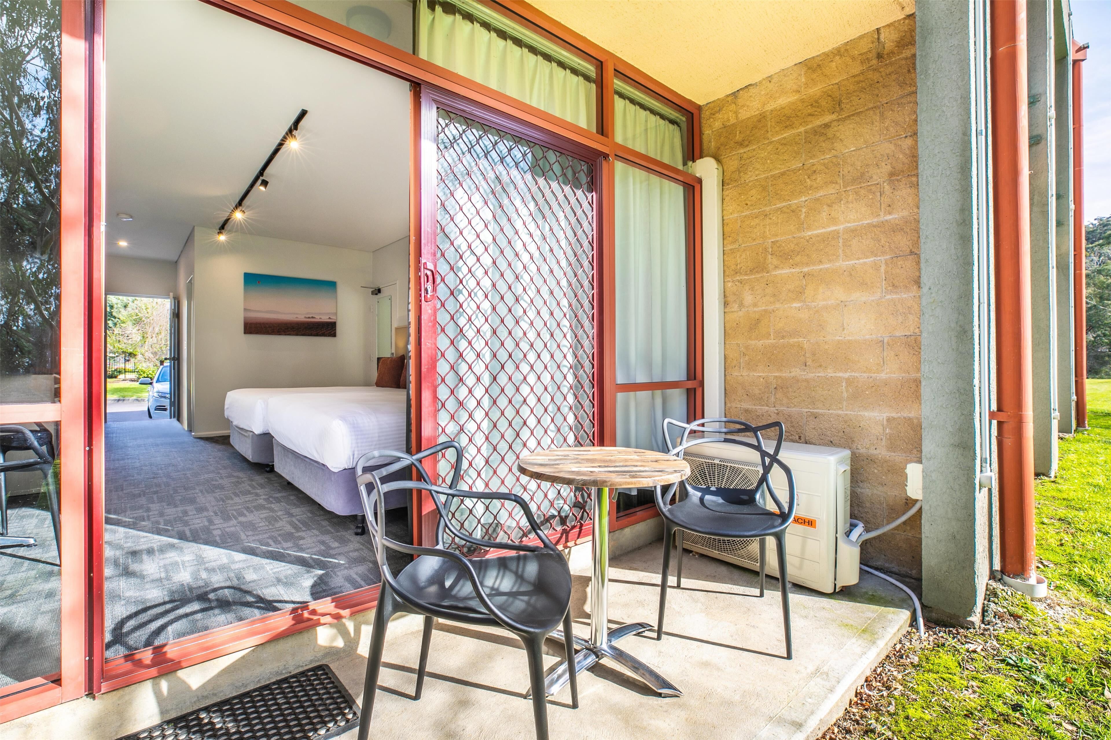 Habitación con cama, una mesa y dos sillas en un balcón con vistas al exterior.