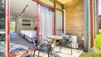 A room with a bed, a table, and two chairs on a balcony with a view of the outdoors.