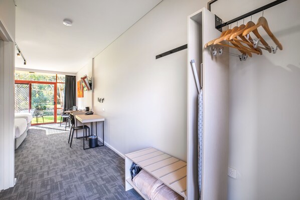 Una habitación moderna con una cama, un escritorio y un banco. Se ve follaje verde a través de la ventana.