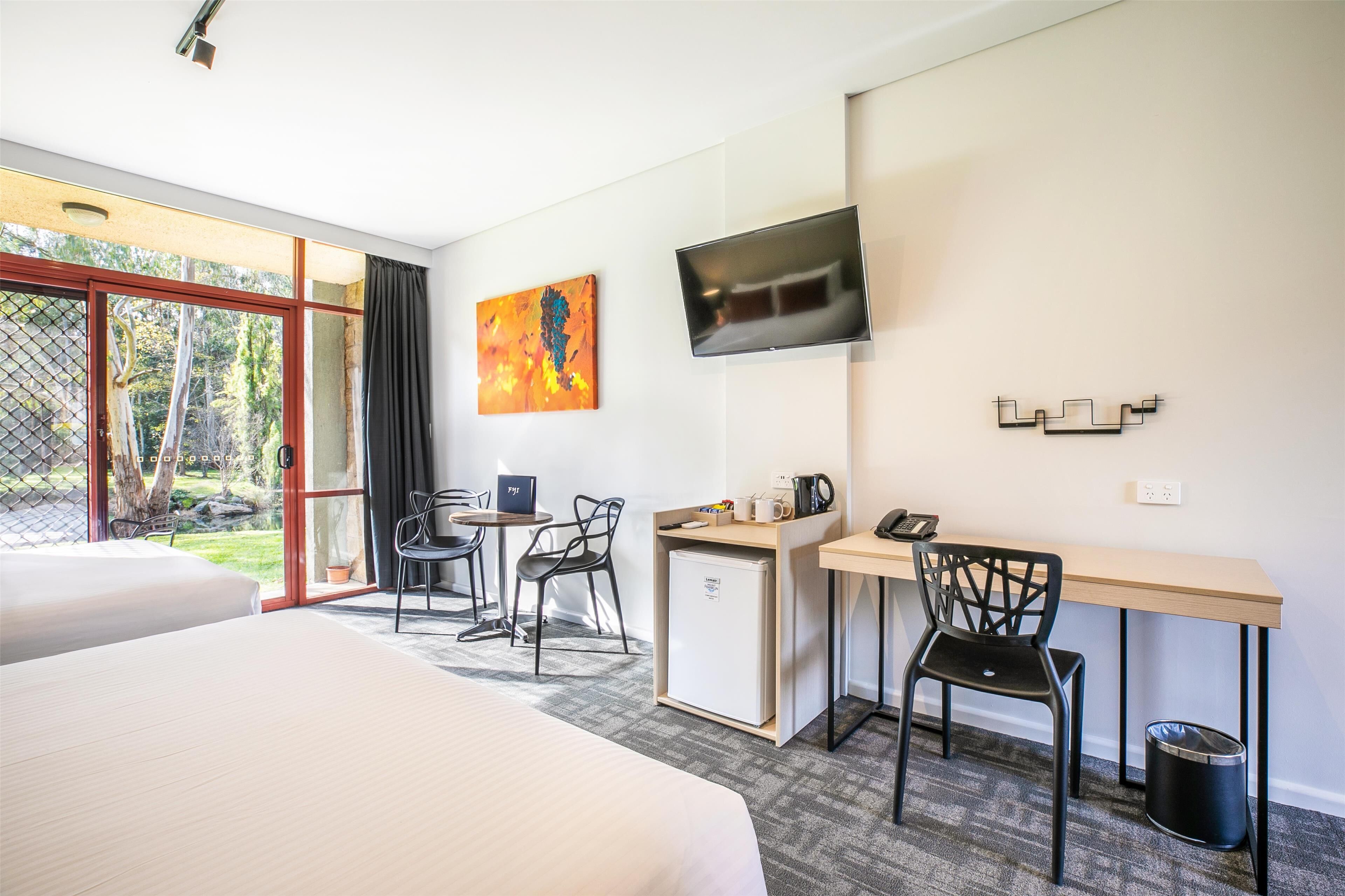 Hotellihuone, jossa on sänky, työpöytä, tuoli, televisio ja taulu seinällä.