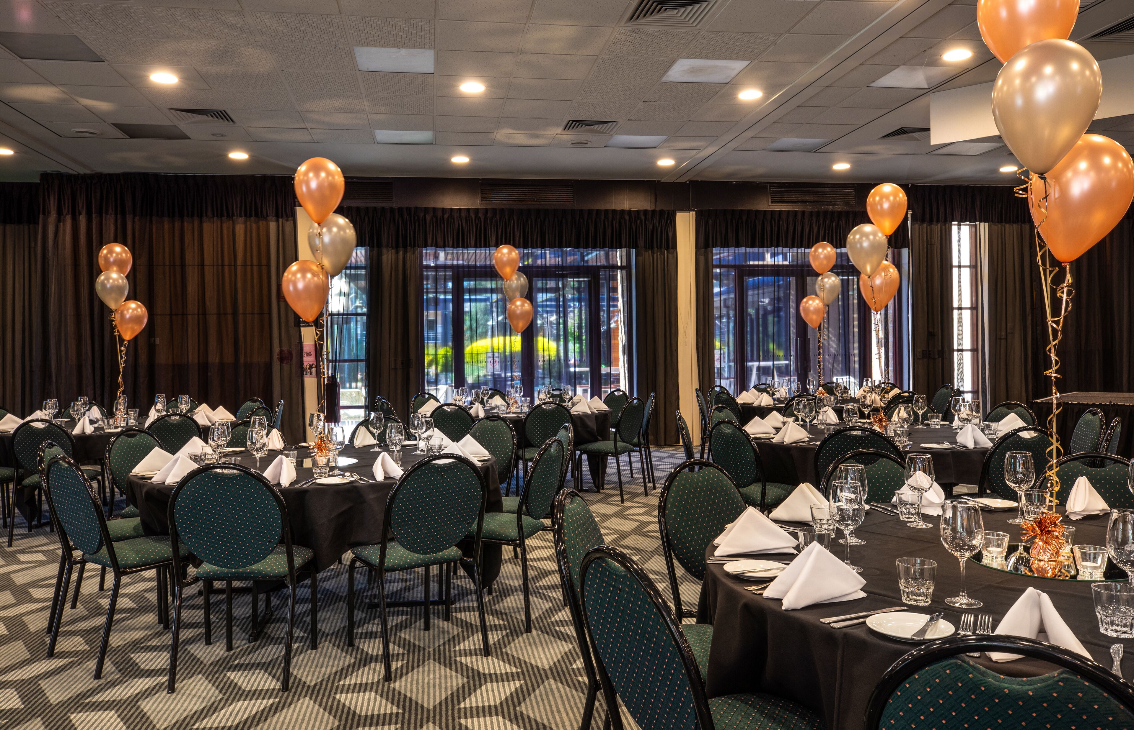 Un salón de banquetes con mesas redondas dispuestas para comer, sillas y vistas al exterior a través de amplias ventanas.