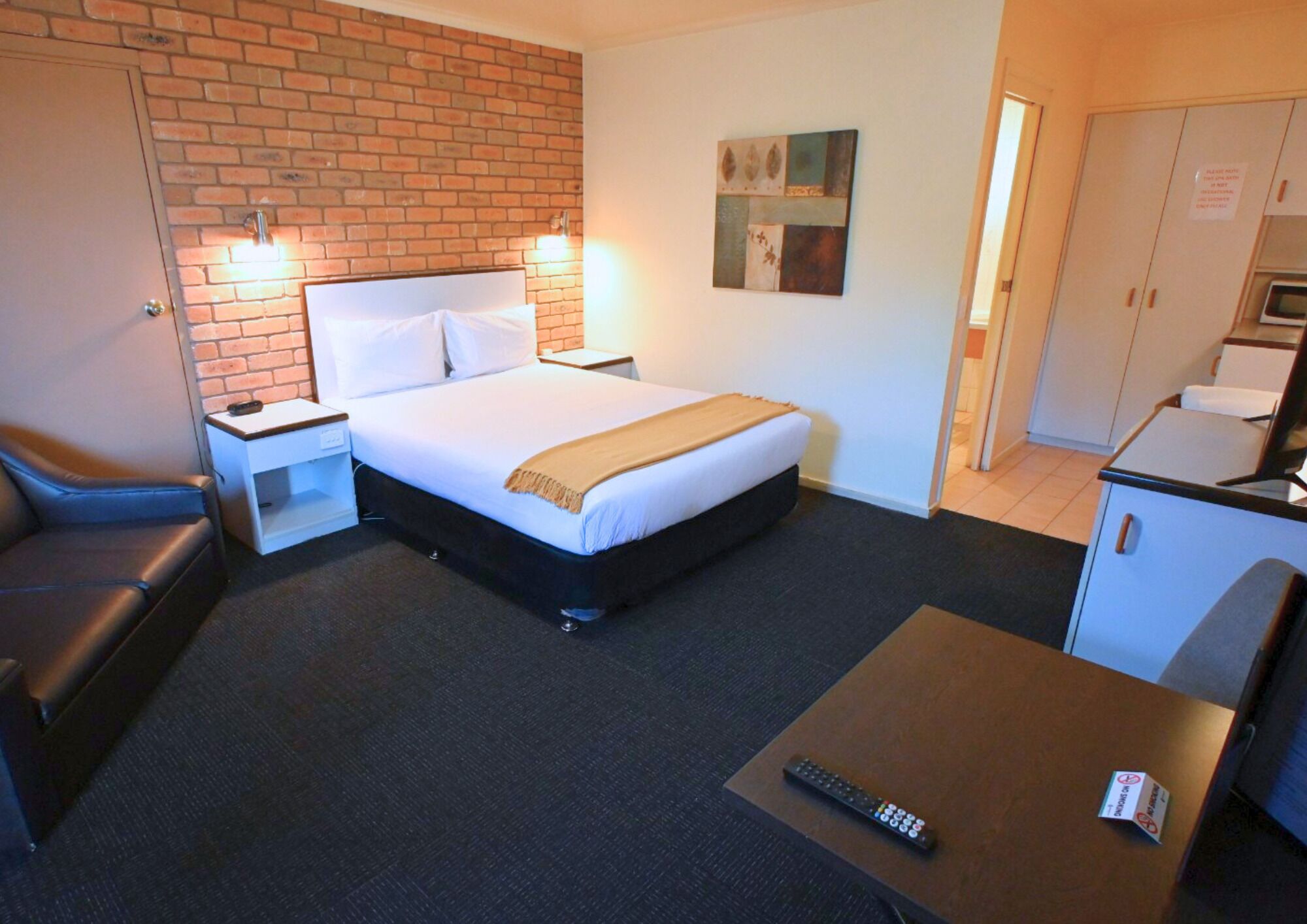A hotel room with a bed, a desk, a chair, a couch, a TV, and a microwave.