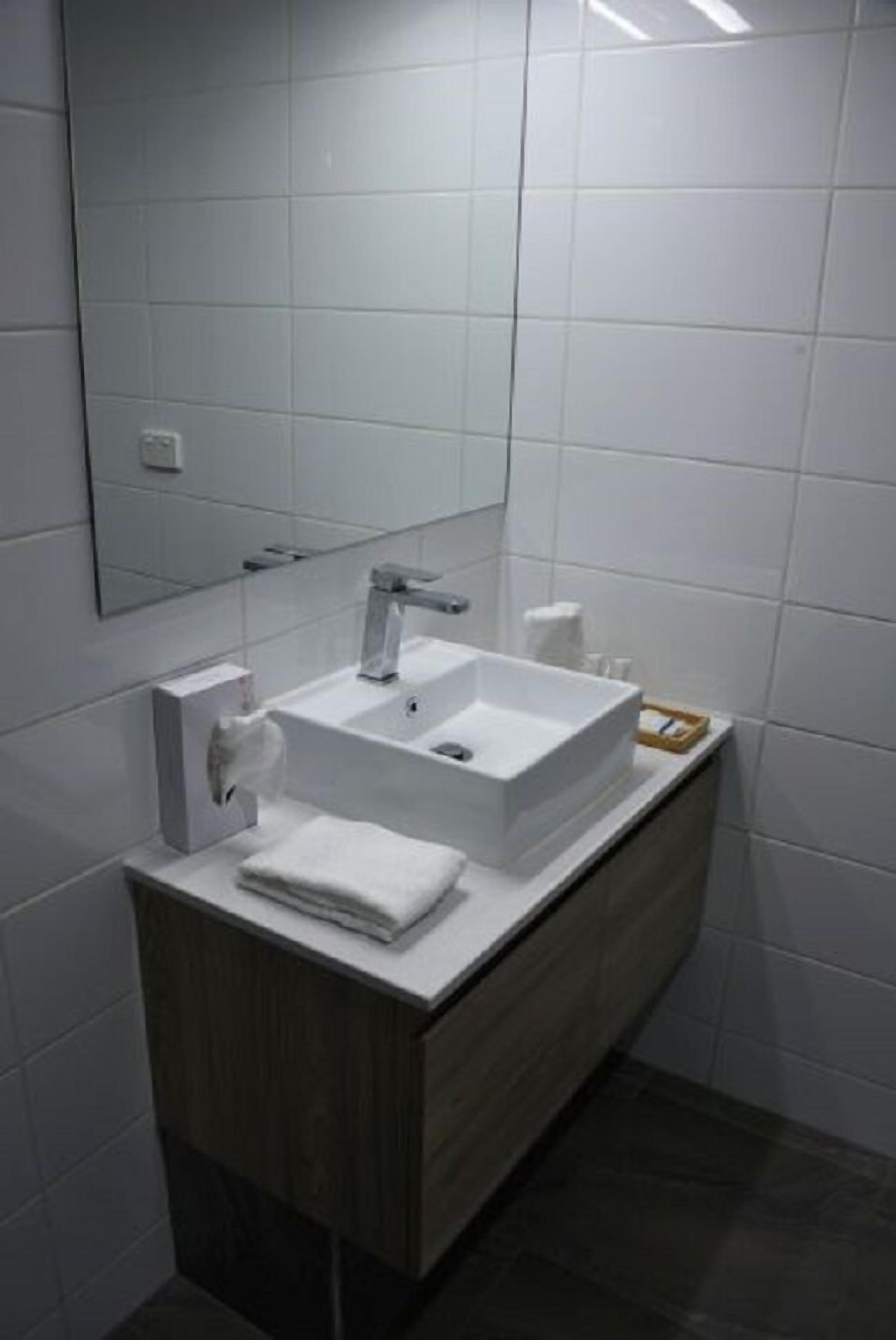 Un baño moderno con un lavabo blanco, espejo y tocador de madera.