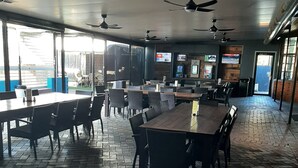 An indoor dining area with brick flooring, tables, chairs, ceiling fans, and large windows. - Peppermill Inn (Kialla)