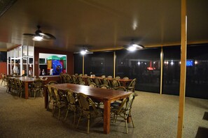 A conference room with multiple tables and chairs, large windows, and ceiling fans.