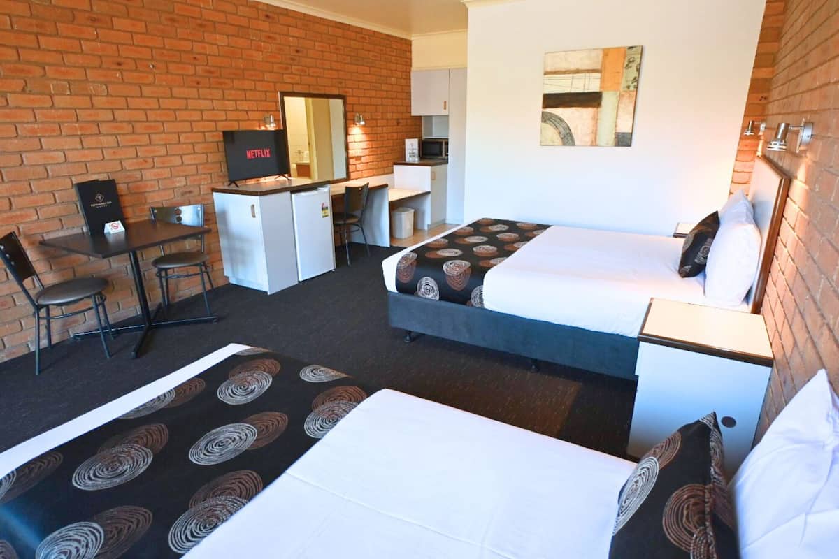 A hotel room with two beds, a desk, a TV, and a brick wall.