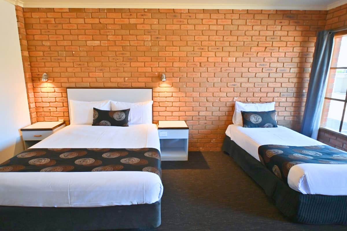 A room with two beds, a brick wall, and a window with curtains.