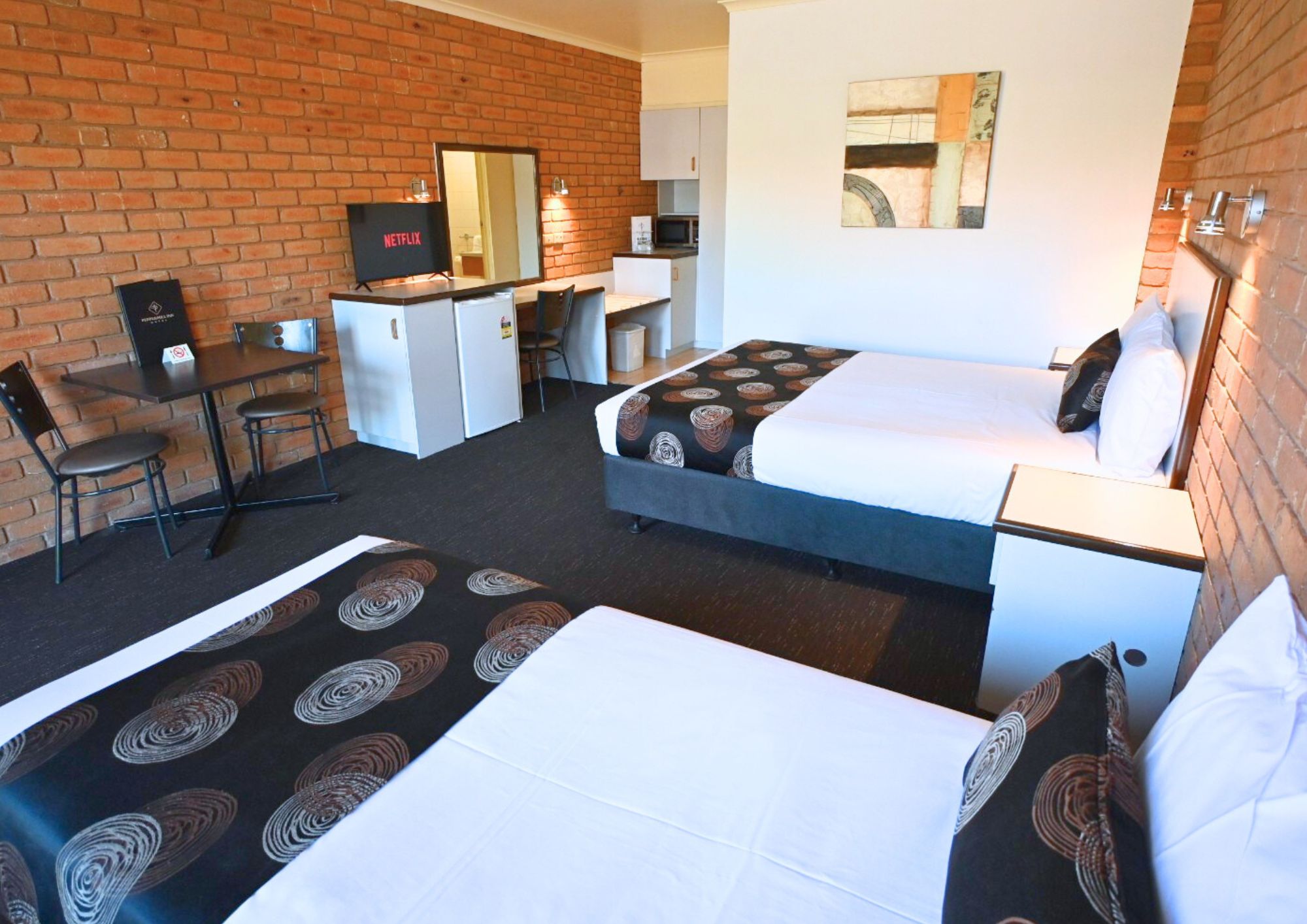 A hotel room with two beds, a desk, a TV, and a brick wall.