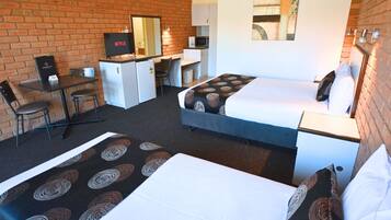 A hotel room with two beds, a desk, a TV, and a brick wall.