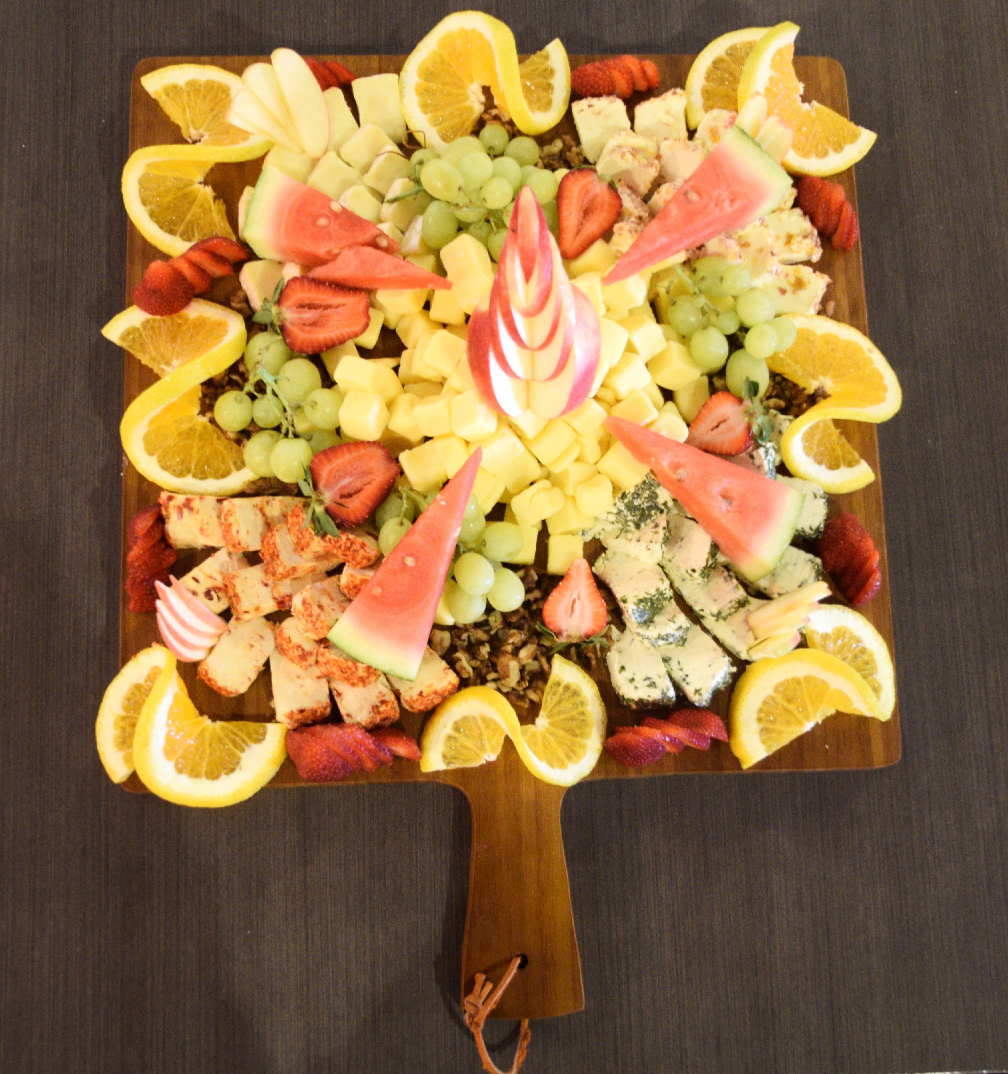 Un tagliere di legno con un'assortimento di frutta e verdura, tra cui fragole, uva e anguria, disposti a formare un motivo decorativo.