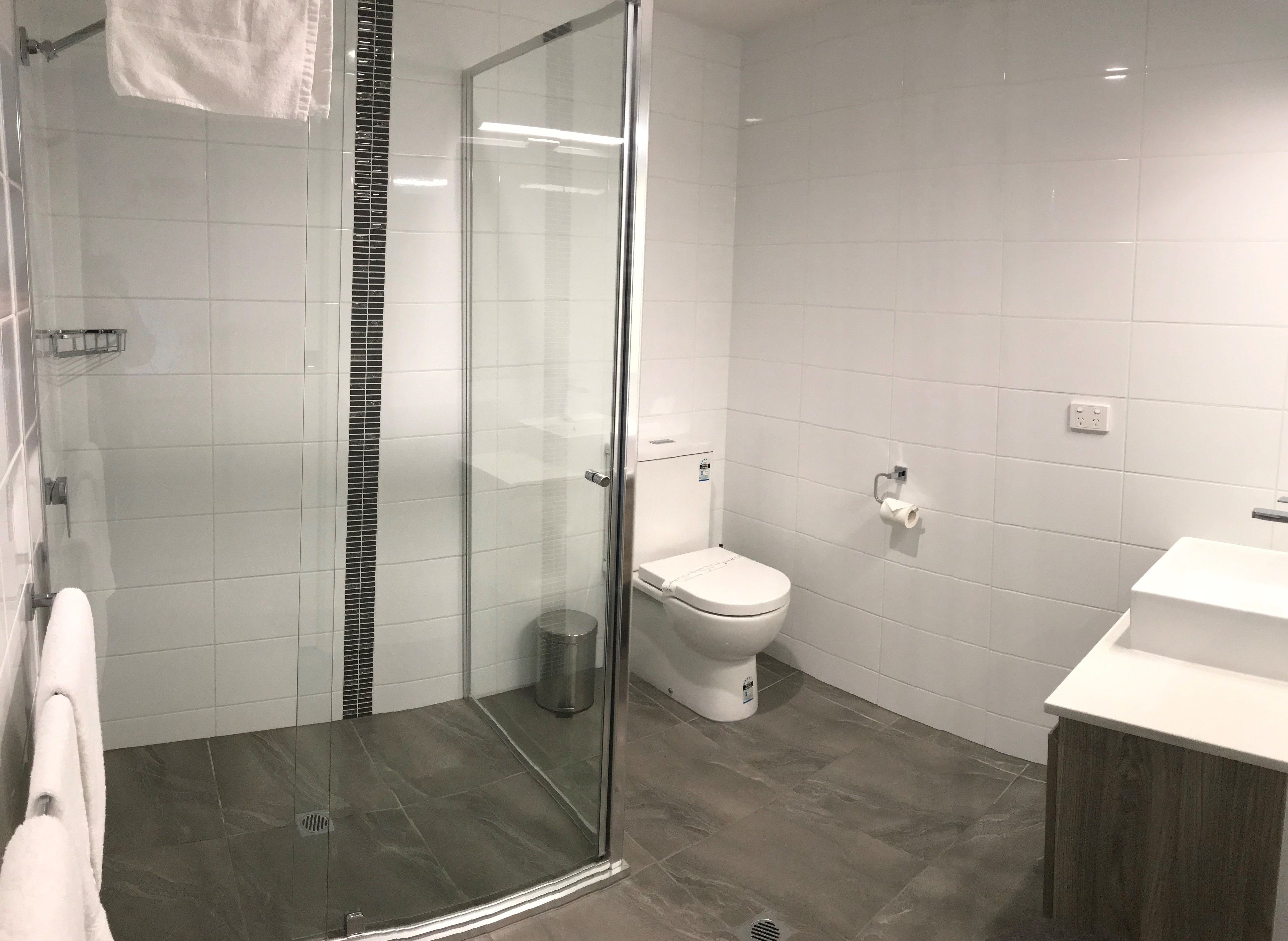 Een moderne badkamer met een douchecabine, toilet en wastafel.