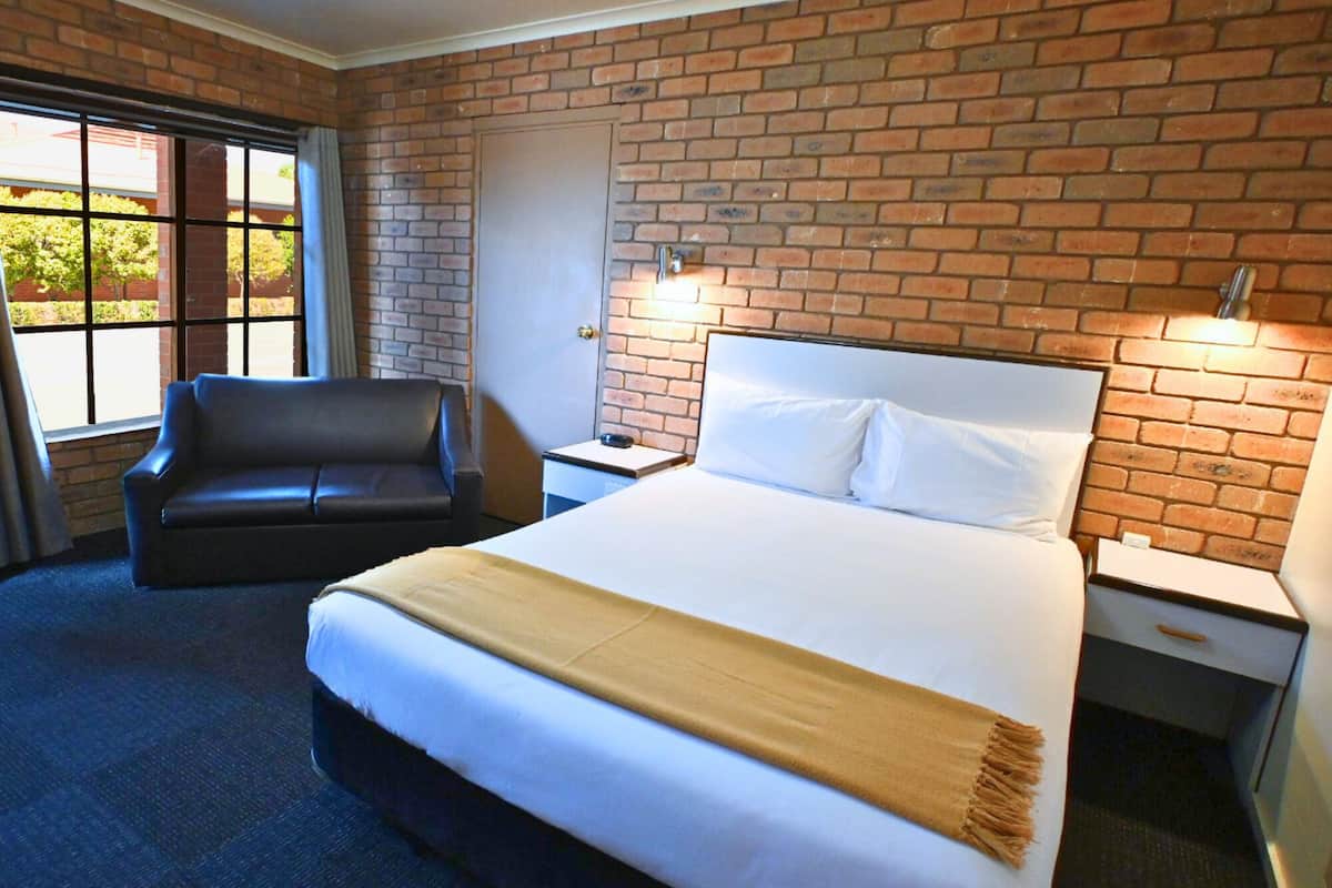 A hotel room with a large bed, a chair, a nightstand, and a brick wall.