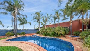 A swimming pool with a curved brick edge, surrounded by palm trees and a brick patio. - Peppermill Inn (Kialla)