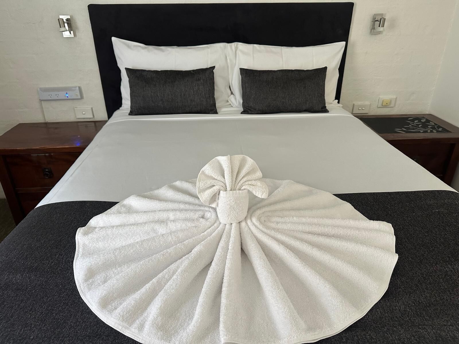 Habitació d'hotel amb un llit ben fet, una taula de nit i una meseta de nit.