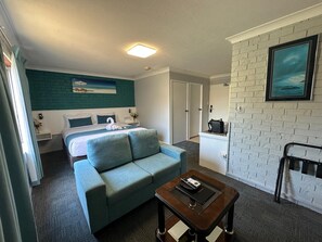 A hotel room with a bed, a blue sofa, a small table, a white brick wall, and a painting.