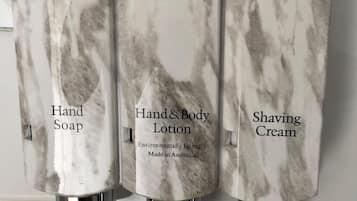 Tres dispensadores de baño etiquetados con diferentes productos: jabón de manos, loción corporal y crema de afeitar.