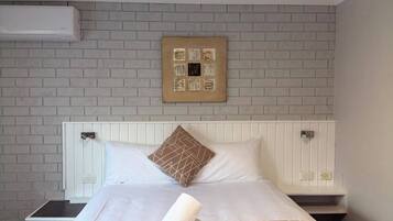 A hotel room with a bed, a white headboard, a brick-patterned wall, and a framed artwork above the bed.