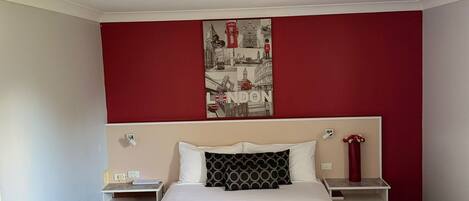 A hotel room with a bed, a nightstand, a red wall, and a London-themed artwork.
